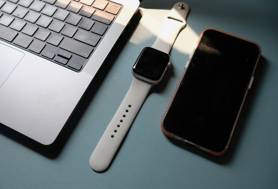 Flat lay of laptop, smartwatch, and smartphone on a blue surface